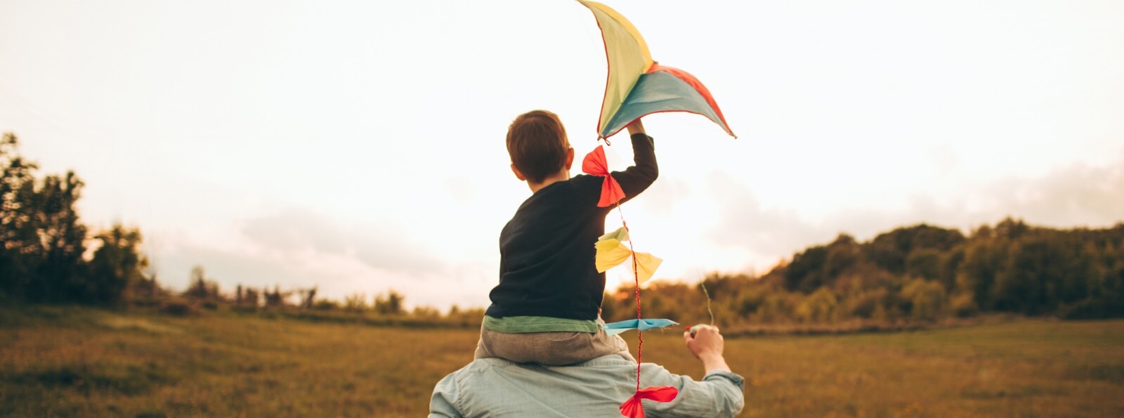 kid holding a kite and riding on a parent's shoulders