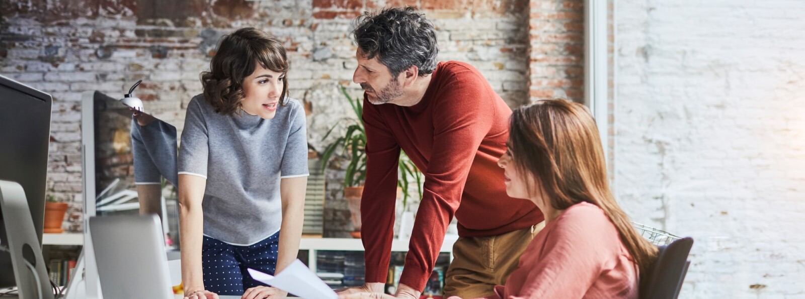 group of professionals talking around a desk with computers